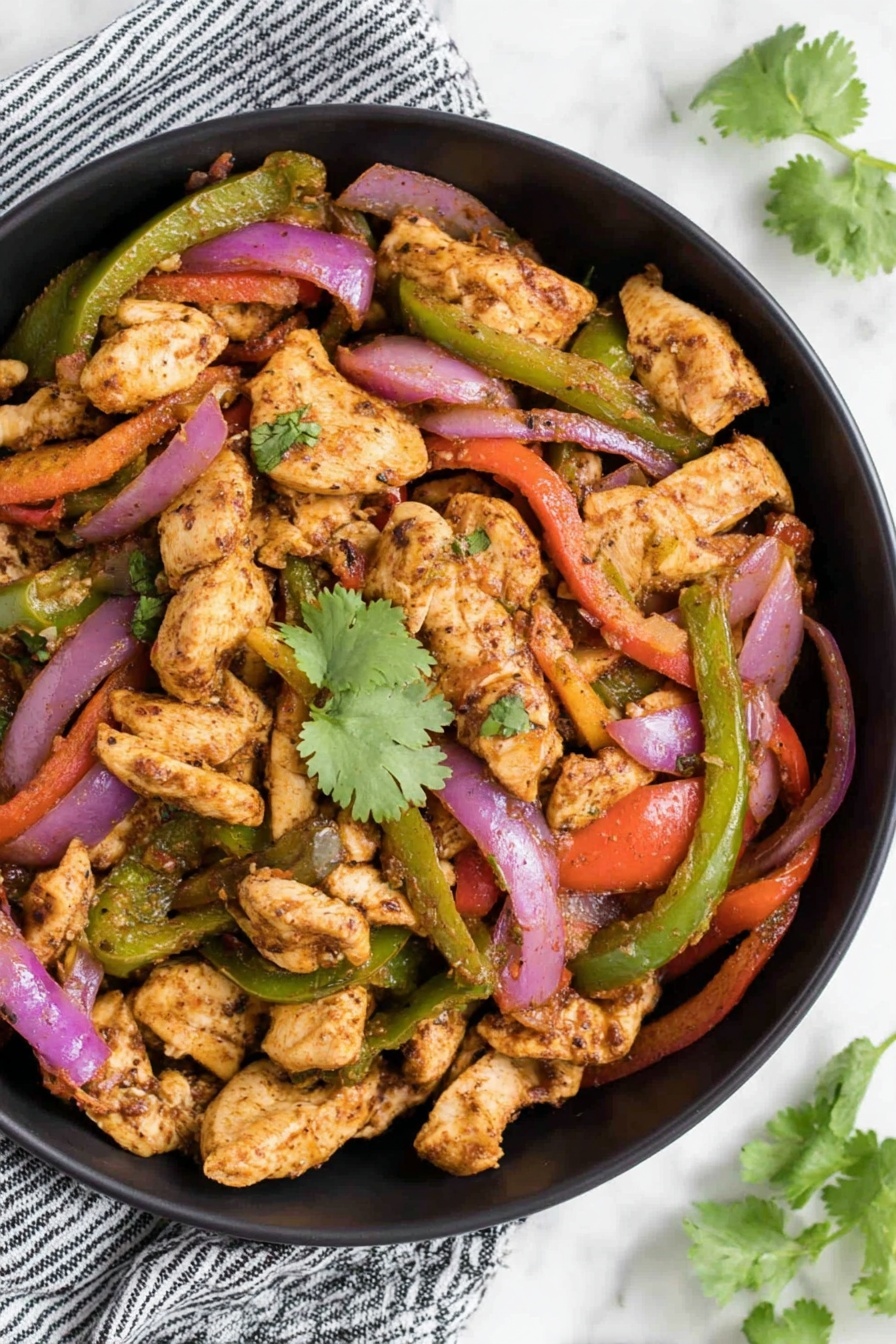 The image shows a black bowl filled with cooked pieces of light brown chicken, mixed with sautéed red and green bell pepper strips, and purple onion slices. The chicken pieces have a slightly browned texture and are scattered throughout the bowl. Bright green cilantro leaves are placed on top as garnish, adding a fresh contrast. The bowl is placed on a white marbled surface with a striped cloth partially visible on one side and some green leaves in the corner. photo taken with an iphone --ar 2:3 --v 7