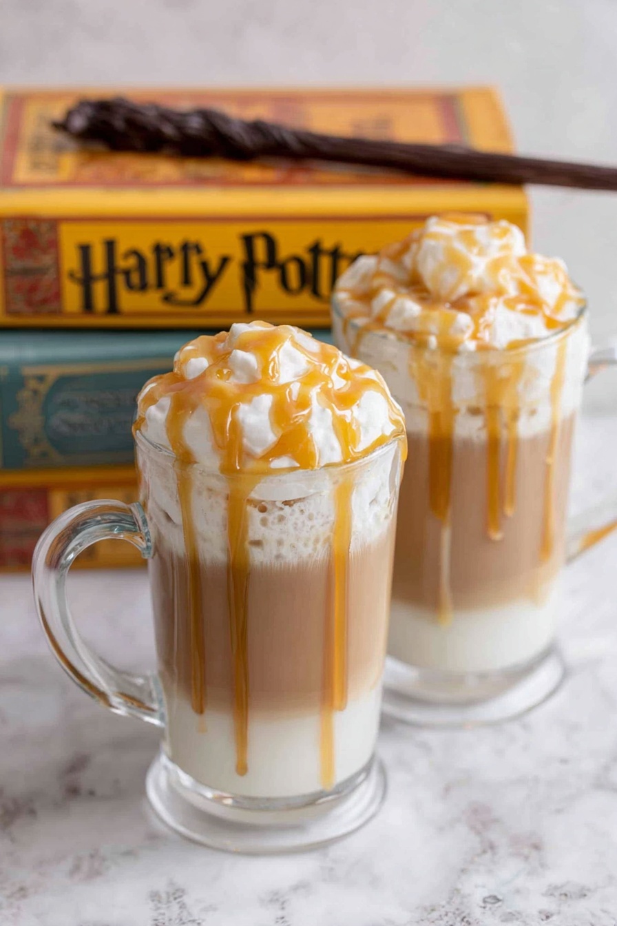 A tall clear glass holds three layers: the bottom layer is light brown creamy tea filling most of the glass, above it is a thin lighter tan layer of foam or froth, and on top is a large fluffy white whipped cream that rises above the glass rim with soft peaks. Caramel sauce with a shiny golden amber color is drizzled over the whipped cream, dripping slightly down the side of the glass. The glass sits on a white marbled surface with blurred warm-colored books in the background. photo taken with an iphone --ar 2:3 --v 7