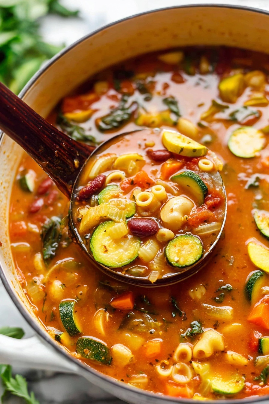 A close-up of a large white pot filled with a thick vegetable soup that has a rich orange-red broth. The soup has many visible layers of colorful vegetables including green zucchini slices, orange carrot cubes, yellow squash, pale onion pieces, dark green leafy bits, and red kidney beans. There are also small pasta shells scattered throughout the soup. A dark wooden ladle is scooping a spoonful of the soup, showing a mix of all these ingredients with the broth. The pot sits on a white marbled surface with some green herbs blurred in the background. The photo has bright natural light highlighting the vibrant colors of the soup. photo taken with an iphone --ar 2:3 --v 7