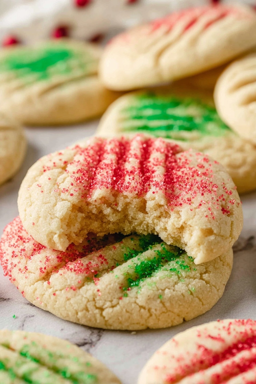 A white plate with a stack of light golden round cookies in the center. Each cookie has a textured pattern of fork marks on top, covered with colored sugar sprinkles, some in green and others in red. The top cookie leans slightly to show its side, revealing soft texture and thickness. Around the stack, more cookies are placed flat on the plate, with red and green sugar sprinkles scattered lightly on the white marbled surface below. The background is softly blurred, focusing attention on the cookies. photo taken with an iphone --ar 2:3 --v 7
