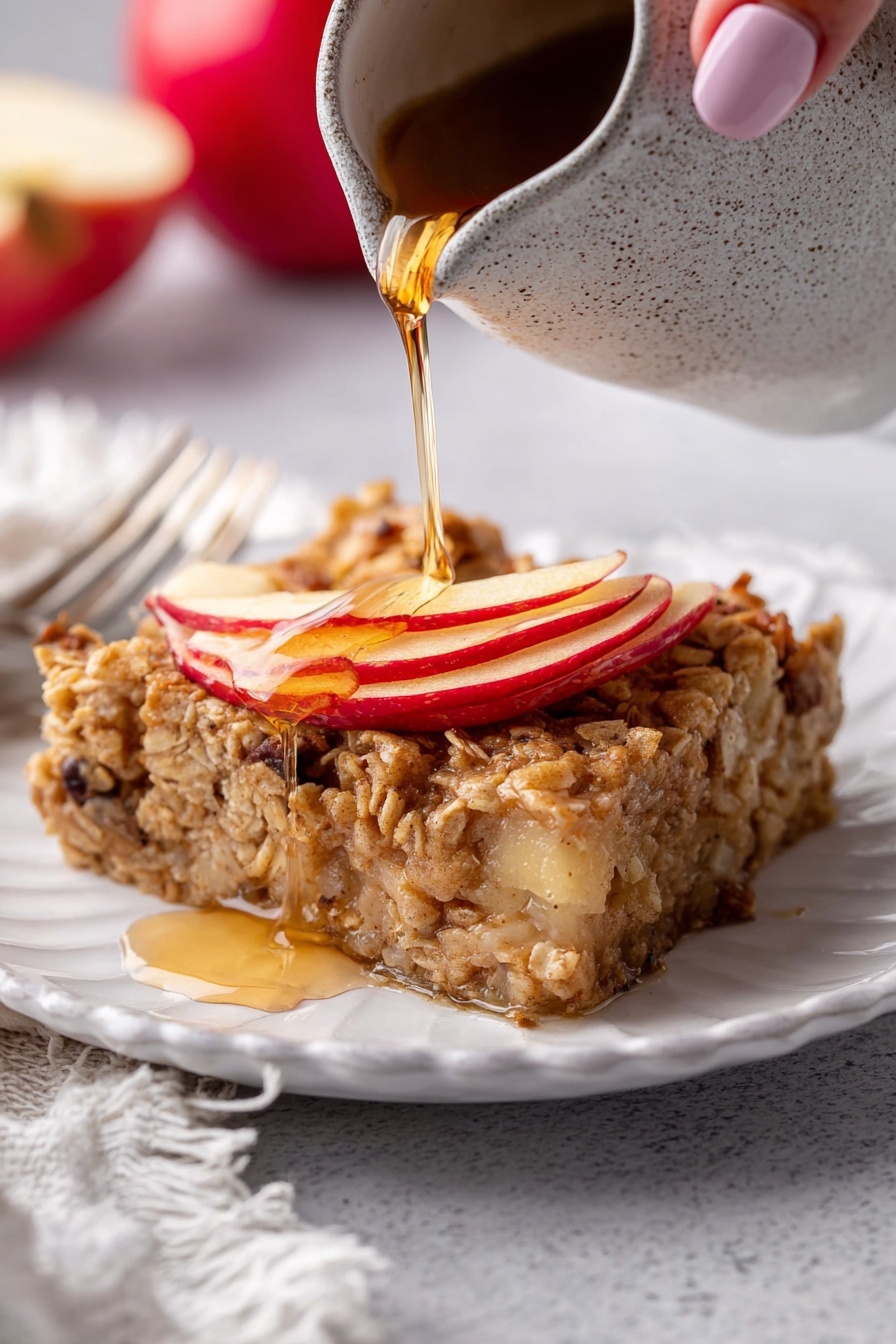 The image shows a white baking dish filled with a baked apple and oat dessert cut into square pieces. The top layer is golden brown and textured, with many small, soft cubes of apple mixed evenly throughout. The apples have reddish and yellowish skin, with some pieces showing a slightly caramelized edge. The oat layer looks moist and spongy, binding the apples together, with hints of cinnamon or spices visible as a light brown color throughout. A silver serving spatula with a floral cut-out pattern rests inside the dish on the right side. The dish is placed on a white marbled surface. photo taken with an iphone --ar 2:3 --v 7