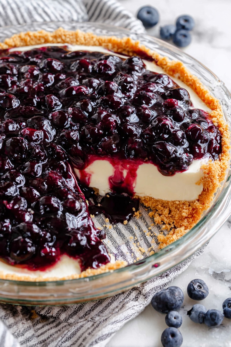 A clear glass pie dish sits on a white marbled surface with a striped cloth underneath. The pie has three visible layers: a light golden crumb crust forming the base and edge, a smooth creamy white middle layer that looks soft and thick, and a top layer of shiny dark purple blueberries covered in a glossy syrup. Part of the pie is missing, showing the contrast between the creamy middle and the juicy berry topping with syrup dripping onto the white marbled surface. Some fresh blueberries are scattered around the dish. Photo taken with an iphone --ar 2:3 --v 7