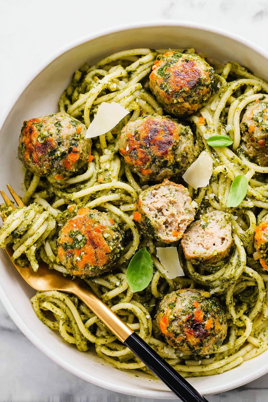 The image shows a white shallow bowl filled with thick spaghetti pasta coated in green pesto sauce, creating a smooth, herbaceous texture that covers every strand. On top of the pasta, there are seven round meatballs that are browned with visible bits of herbs and orange carrot pieces mixed in, adding a rough and varied texture. Scattered around the bowl are small green basil leaves and thin, flat shavings of pale white cheese. The background is a white marbled surface, with a small white dish of green pesto and another white dish with more cheese shavings partially visible at the bottom and right side of the image. photo taken with an iphone --ar 2:3 --v 7
