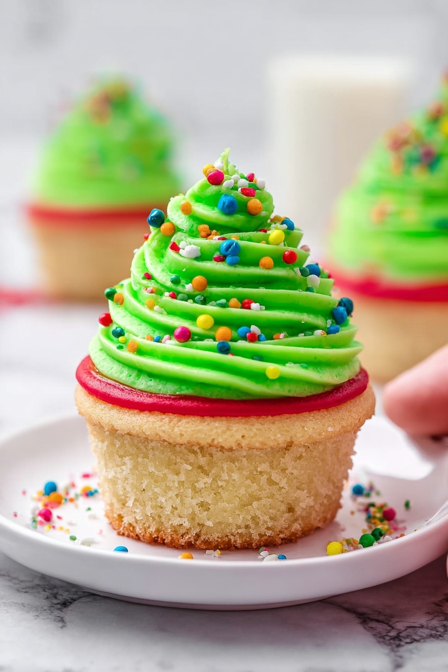 This image shows a single cupcake on a white marbled surface, with a green cupcake liner partially peeled down. The cupcake has a light beige cake base topped with a bright red icing ring, then a thick swirl of bright green frosting spiraled on top. The green frosting is decorated with round, colorful sprinkles in red, blue, orange, and green, adding bright pops of color. There is a light dusting of white powdered sugar over the frosting and the red icing ring. Scattered colorful sprinkles surround the cupcake on the surface. Photo taken with an iphone --ar 2:3 --v 7