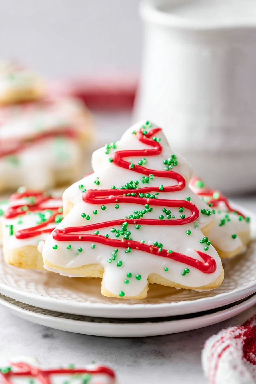 A close-up view of a white Christmas tree shaped cookie covered with smooth white icing sprinkled with small green sugar crystals, decorated with wavy red icing lines across the surface. The cookie is placed on a stack of white plates with other similarly decorated cookies visible in the background. The background has a soft white marbled texture, and the scene includes a blurred white cup behind the plates. The overall look is clean, festive, and bright, emphasizing the holiday colors of red, green, and white. Photo taken with an iphone --ar 2:3 --v 7