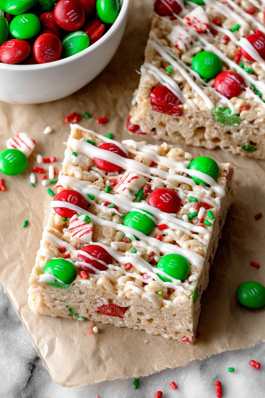 The image shows two thick square bars made from a light beige cereal base with a slightly bumpy texture. Each bar is decorated with red and green candy-coated chocolates placed unevenly across the top, standing out with their shiny surfaces. There are small red and green sprinkles scattered on and around the bars. A white drizzle, likely icing, is spread in uneven lines over the tops of the bars and the white marbled surface beneath. A white bowl filled with matching red and green candy-coated chocolates is partially visible in the lower left corner. The bars rest on a piece of light brown parchment paper. Photo taken with an iphone --ar 2:3 --v 7
