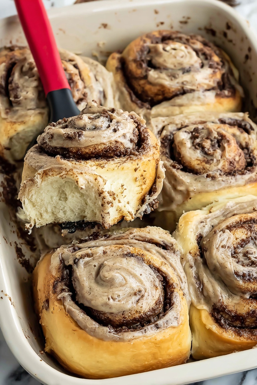 The image shows six cinnamon rolls in a white baking pan, with one roll being lifted out by a red and black spatula. Each roll has three visible layers: a golden-brown outer dough layer with a soft, fluffy texture, a dark brown cinnamon filling layer in the middle that looks rich and moist, and a thick light brown cream cheese frosting layer with specks of cinnamon spread on top and swirled inside the roll. The background is a white marbled surface, and there is some cinnamon filling residue around the edges of the pan. Photo taken with an iphone --ar 2:3 --v 7