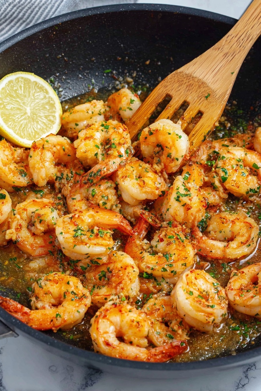 A close view of a black pan filled with cooked shrimp that are orange with white accents, showing a slightly curled shape. The shrimp are coated in a light brown sauce and sprinkled with small green herb pieces. A wedge of lemon with a bright yellow peel and pale yellow inside rests on the left side of the pan. A wooden spatula touches the shrimp on the right side, mixing them gently. The pan sits on a white marbled surface. photo taken with an iphone --ar 2:3 --v 7