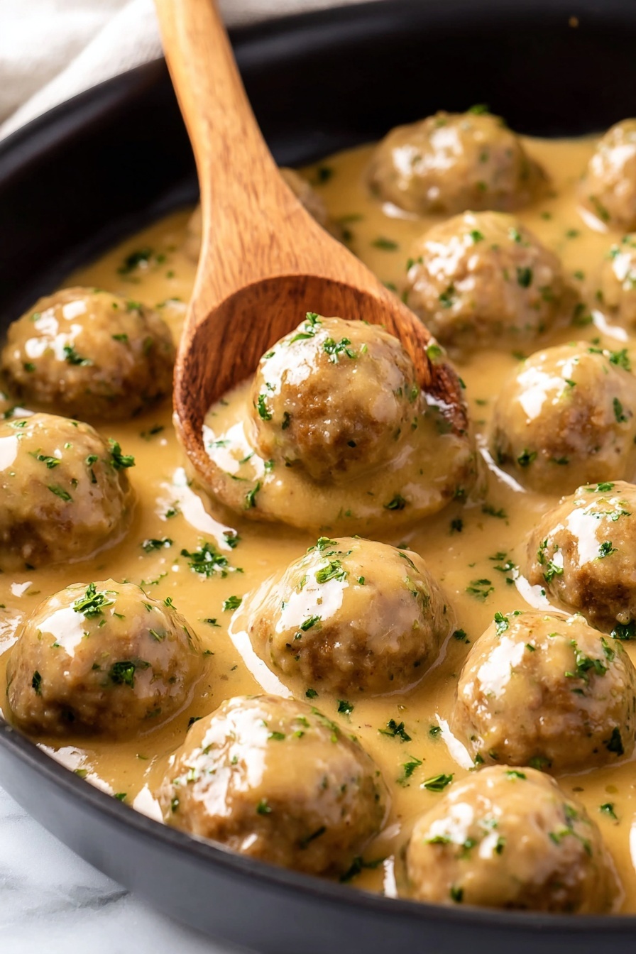 The image shows a close-up of a black pan filled with smooth, round meatballs covered in a thick light brown sauce speckled with small green herb bits. A wooden spoon with a flat, wide tip stirs one meatball near the center, lifting it slightly. The sauce has a glossy texture, coating each meatball evenly and pooling gently around them. The pan rests on a white marbled surface. Photo taken with an iphone --ar 2:3 --v 7