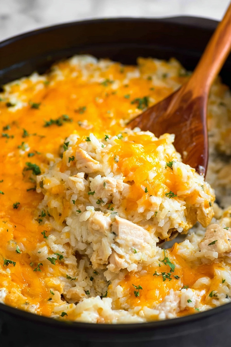 This image shows a close-up of a cooked rice and cheese casserole in a black pot. The dish has one main layer of cooked white rice mixed with pieces of chicken or similar light meat, topped with a bright orange melted cheddar cheese layer that looks slightly bubbly. Small green herbs are sprinkled on top, adding color contrast. A wooden spatula is scooping out some of the casserole, showing the soft texture of rice and melted cheese inside. The background is a white marbled texture. photo taken with an iphone --ar 2:3 --v 7