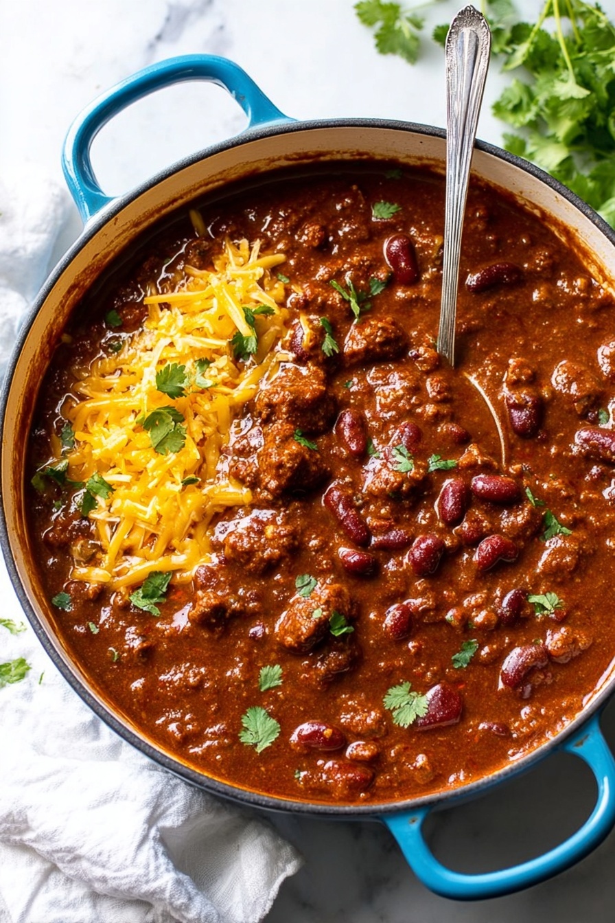 A large round blue pot filled with thick chili showing layers of dark red beans and chunks of brown meat in a rich, slightly glossy brown sauce. On the left side, there is a layer of shredded yellow cheddar cheese and a dollop of white sour cream on top. Small fresh green cilantro pieces are sprinkled across the chili. A shiny silver ladle rests inside the pot, partially submerged in the chili, with some chili on its surface. The pot sits on a white marbled surface with a white cloth nearby and green cilantro leaves in the upper right corner. Photo taken with an iphone --ar 2:3 --v 7