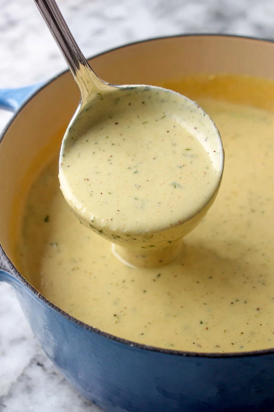 A close-up of thick, creamy sauce with a pale yellow color and small specks of black pepper and herbs, being lifted by a silver ladle inside a blue enamel pot. The sauce has a smooth texture with visible seasoning throughout, filling the pot almost to the brim. The background and surface are changed to a black marbled texture. photo taken with an iphone --ar 2:3 --v 7