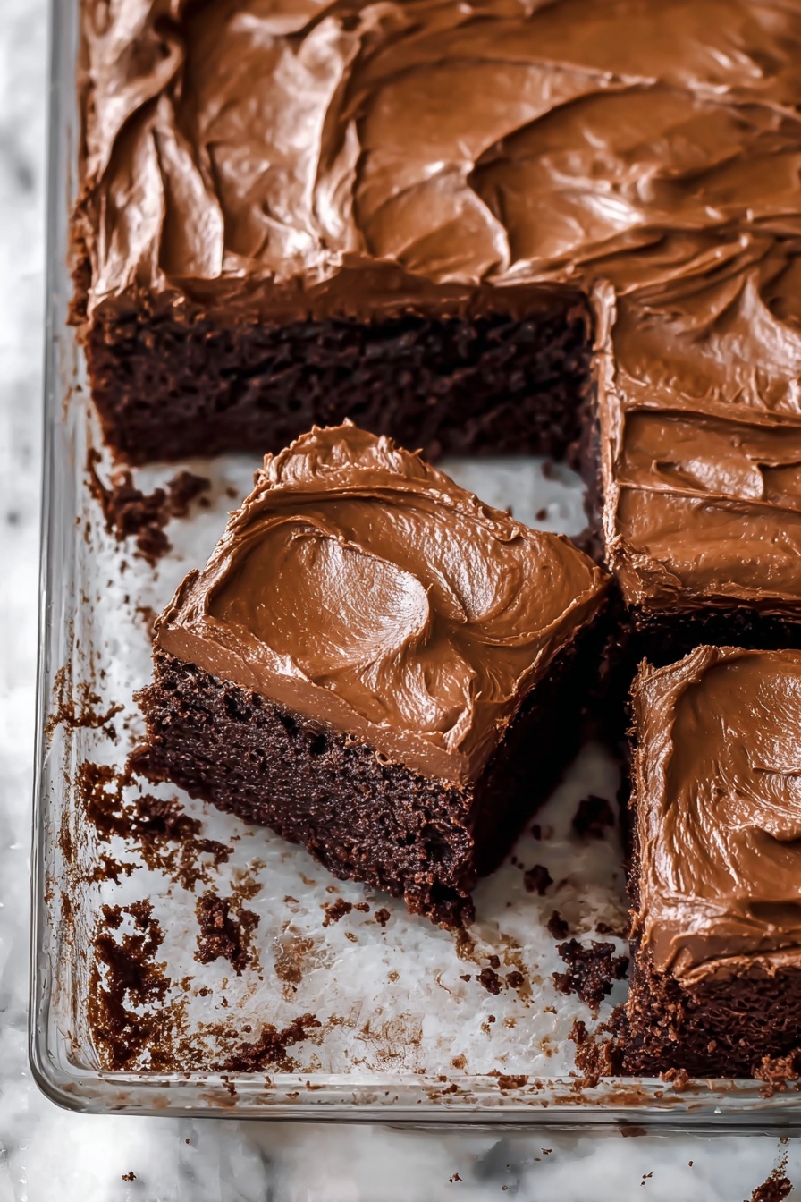 A glass tray holds a rich, dark brown cake with a thick, smooth layer of lighter brown frosting on top that has soft swirls and peaks. Three square pieces have been cut from the cake, showing the dense, moist texture of the dark cake underneath the glossy, creamy frosting. The cake sits on a white marbled surface with some crumbs around the tray edges. photo taken with an iphone --ar 2:3 --v 7