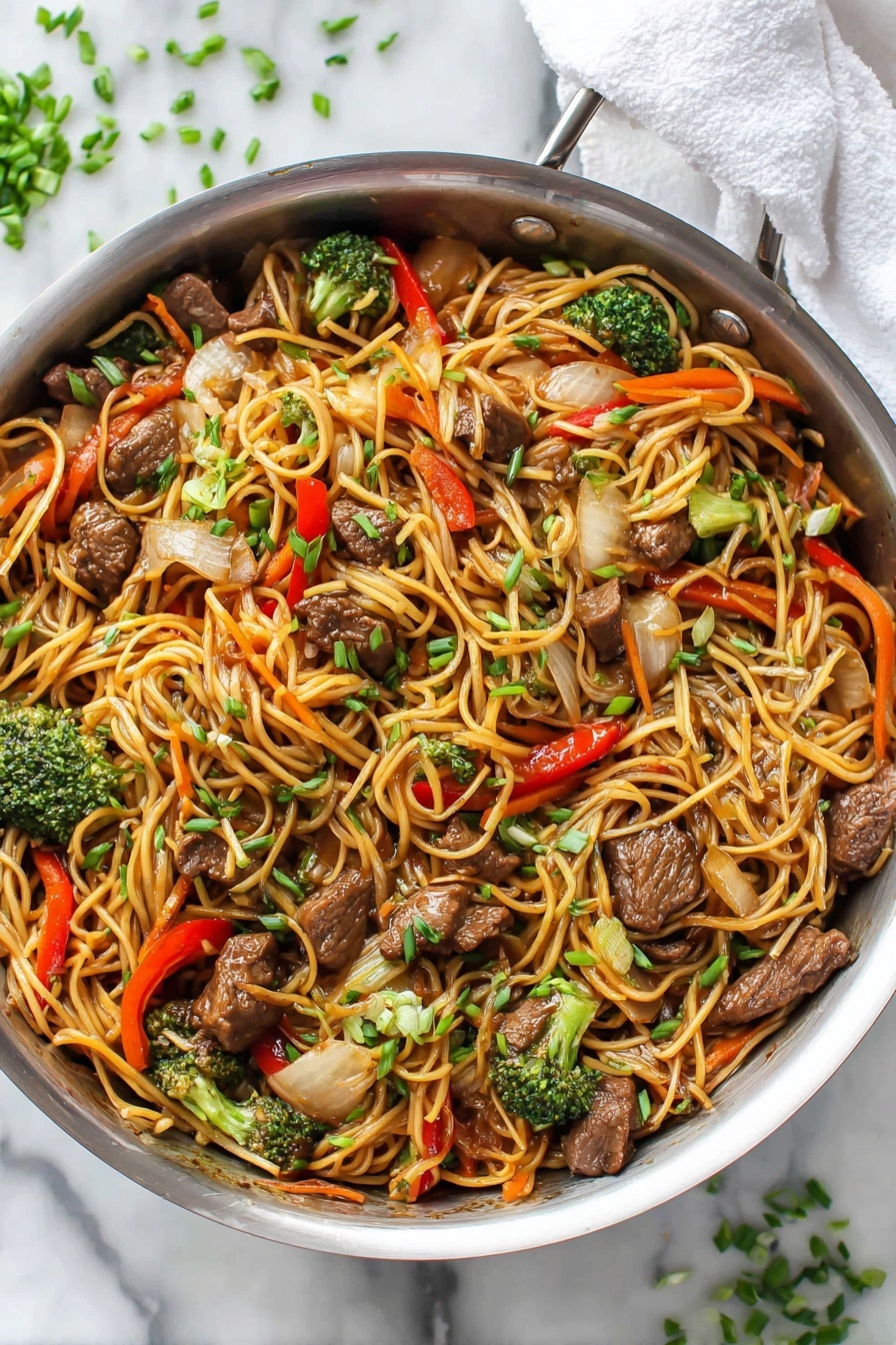 A large silver pan filled with stir-fried noodles mixed with several layers of ingredients: thin, long, light brown noodles forming the base layer, scattered with medium-sized dark brown beef pieces, small bright green broccoli florets, chunks of white onion, strips of orange carrot, and pieces of red bell pepper. All ingredients are mixed and coated with a light glossy sauce, topped with small green chopped chives sprinkled evenly over the dish. The pan is placed on a white marbled textured surface with some chopped green chives scattered nearby and a white cloth partially visible at the top right corner. Photo taken with an iphone --ar 2:3 --v 7