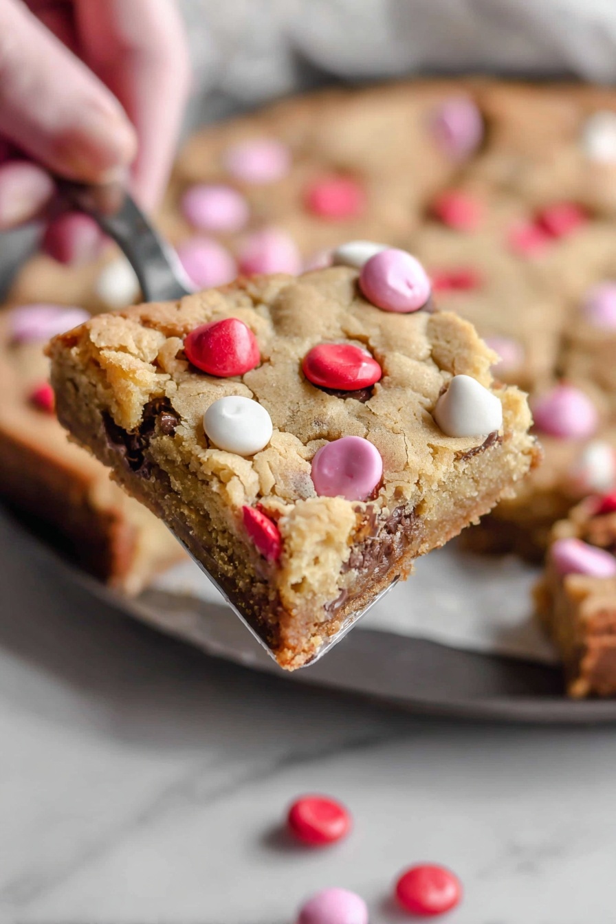 The image shows a close-up of cookie dough with chocolate chips mixed with red, white, and pink candy-coated chocolates scattered on top. The cookie dough is light tan with small dark chocolate chips spread throughout. The candies are round and glossy, with some stacked and resting on the dough’s uneven, soft texture. The background has a white marbled texture that blurs softly out of focus. photo taken with an iphone --ar 2:3 --v 7