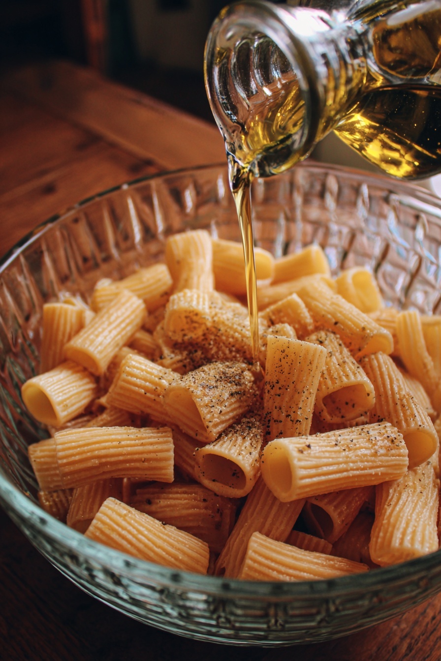 A close-up image of a white bowl filled with golden crunchy ridged pasta chips sprinkled with green herbs and Parmesan cheese. At the center inside the bowl is a smaller white bowl with a thick, red tomato sauce. A woman's hand is dipping one pasta chip into the sauce. The background features a white marbled texture. Photo taken with an iphone --ar 2:3 --v 7