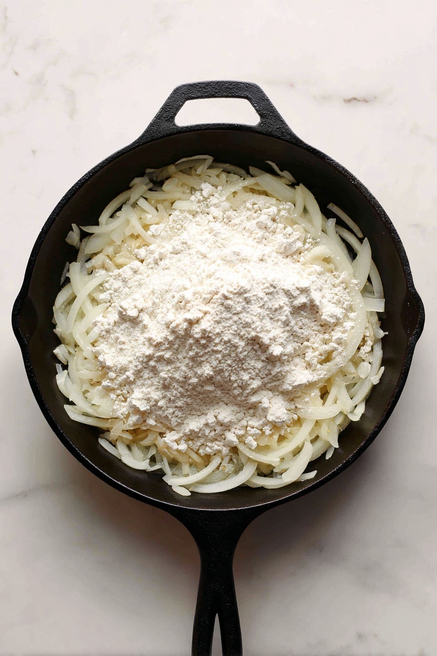 A white bowl filled with three browned sausages placed on top of creamy mashed potatoes, all covered with a light brown onion gravy with visible onion slices and chopped green herbs sprinkled on top. On one side of the bowl is a generous serving of bright green peas. The mashed potatoes have a smooth texture, and the peas appear fresh and round. The bowl sits on a white marbled surface with a silver fork and knife nearby. Photo taken with an iphone --ar 2:3 --v 7